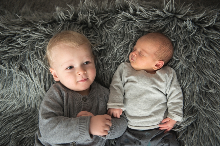 Neugeborenes Baby mit Geschwister Bruder 18 Monate alt liegend auf dem Teppich