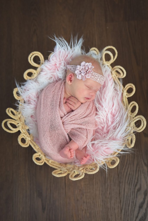 Baby mit rosa Kopfband und rosa Tuch liegt schlafend im Korb
