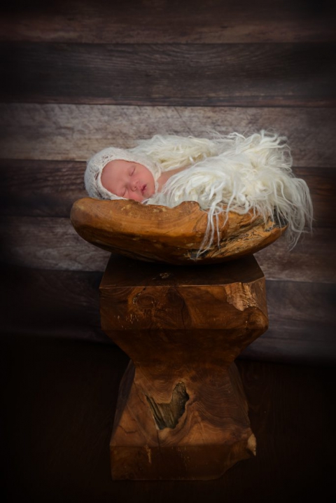 Baby mit Mütze liegt im Holzkorb mit Wollfell