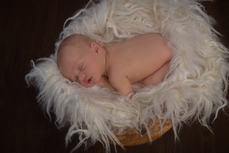 Baby liegt nackt in kuscheliges Nest aus Wolle